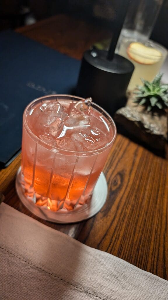 a glass with a drink and ice on a table