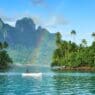 a couple in a boat on a body of water with trees and mountains in the background