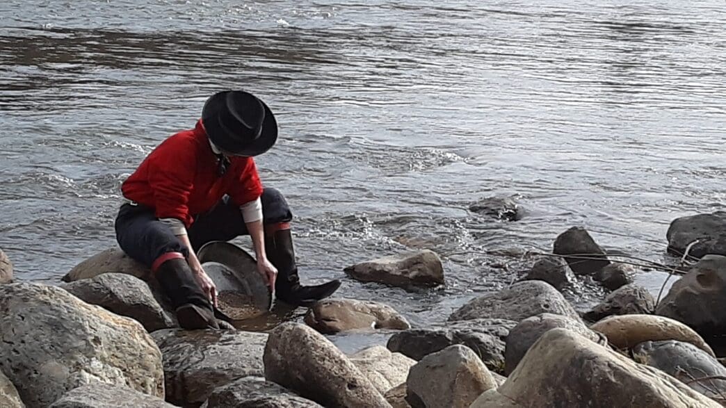 a person in boots and hat cleaning rocks in water