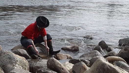 a person in boots and hat cleaning rocks in water