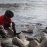 a person in boots and hat cleaning rocks in water