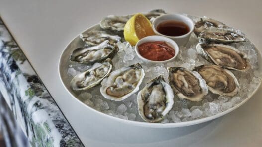 a plate of oysters on ice with sauces and lemon