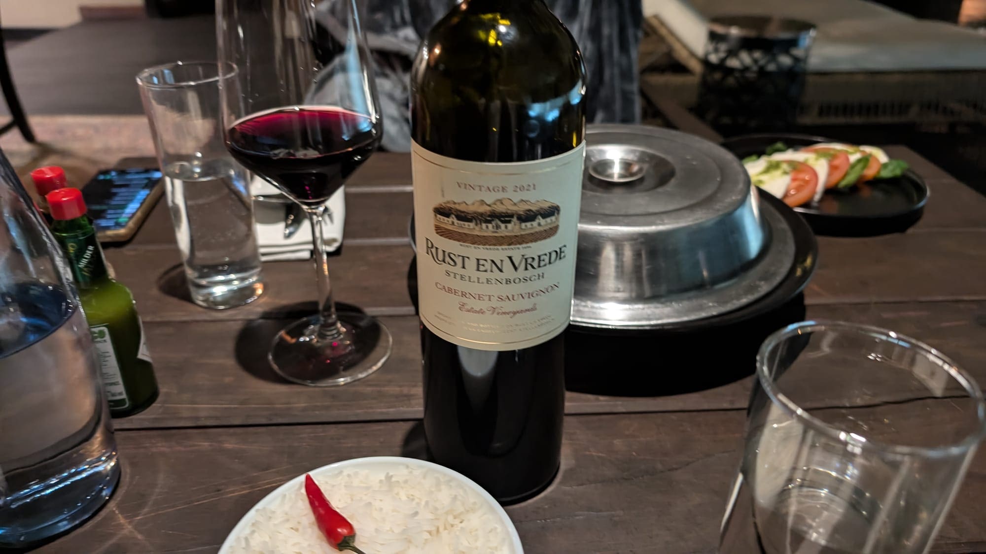 a bottle of wine next to a bowl of rice and a chili pepper