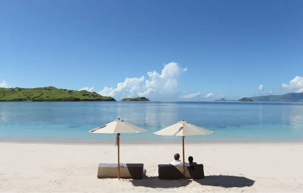 two people sitting on a beach with umbrellas