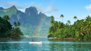 a person in a boat on a body of water with a rainbow in the background