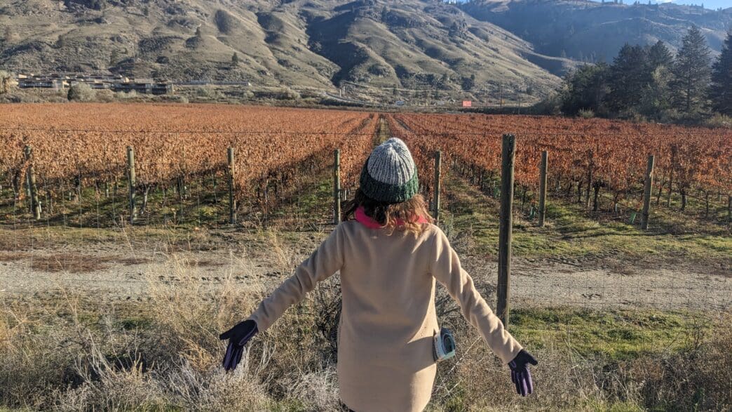 a woman standing in front of a field of vines