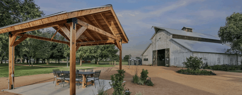 a wooden structure with a table and chairs in front of a barn
