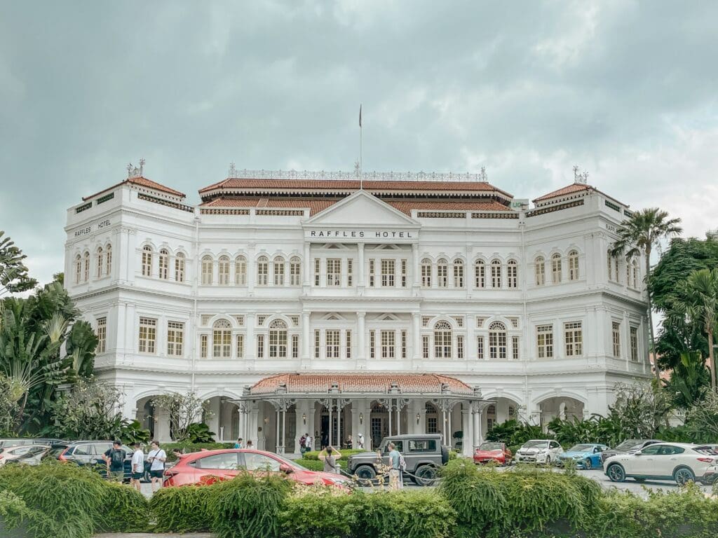a large white building with many windows and cars parked in front with Raffles Hotel in the background