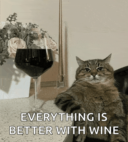 a cat sitting on the floor next to a glass of wine