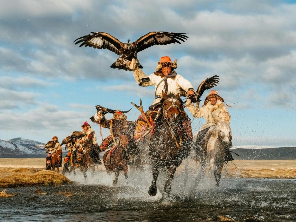a group of men riding horses with birds in the air in Mongolia.