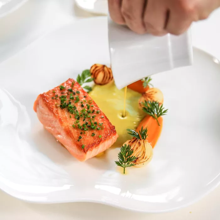 a person pouring sauce onto a piece of food