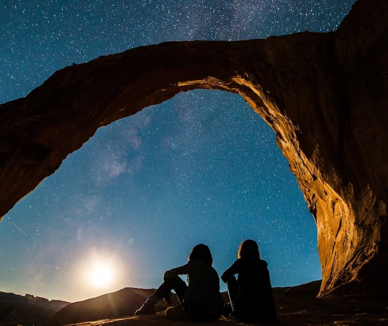 two people sitting under a large rock arch