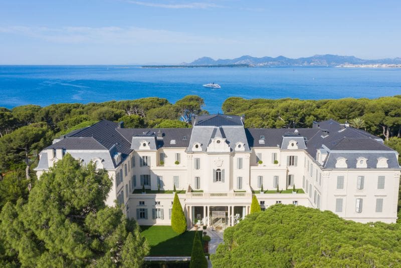 a large white building with trees and a body of water in the background