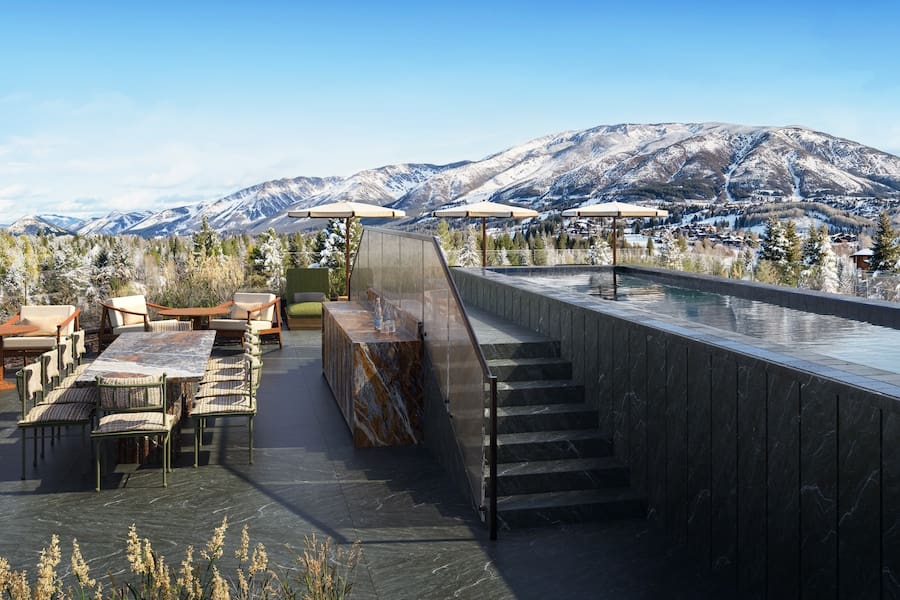 a rooftop patio with a pool and chairs and a mountain range in the background