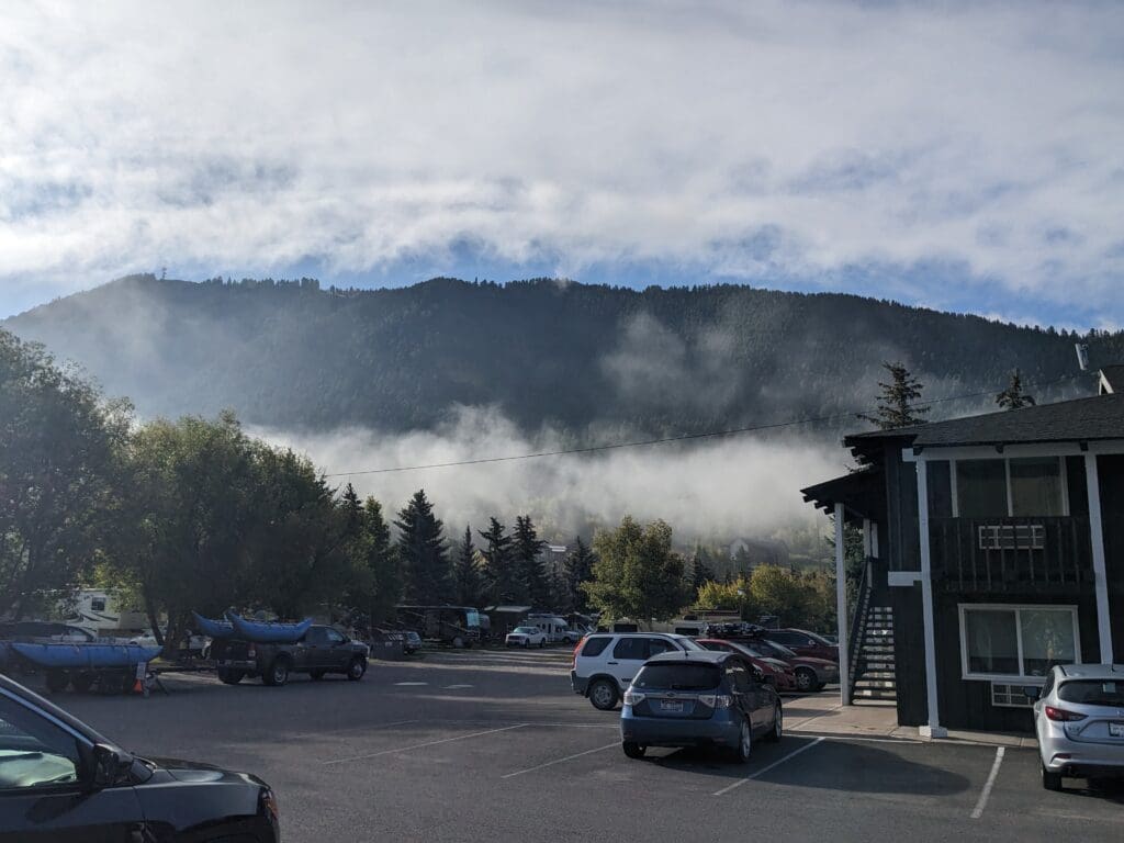 a parking lot with cars and trees in front of a mountain