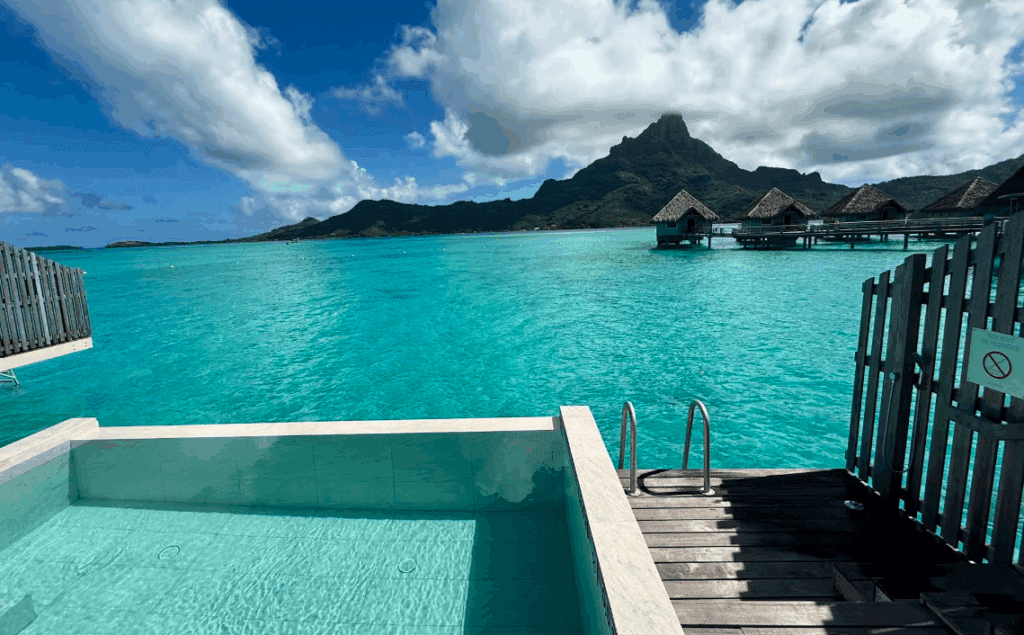 a pool with a hut over water and a mountain in the background