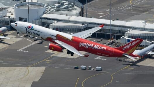 a red and white airplane flying over a runway