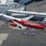 a red and white airplane flying over a runway