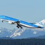 a blue and white airplane flying over mountains