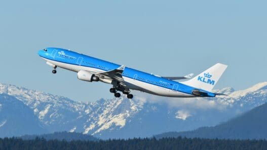 a blue and white airplane flying over mountains