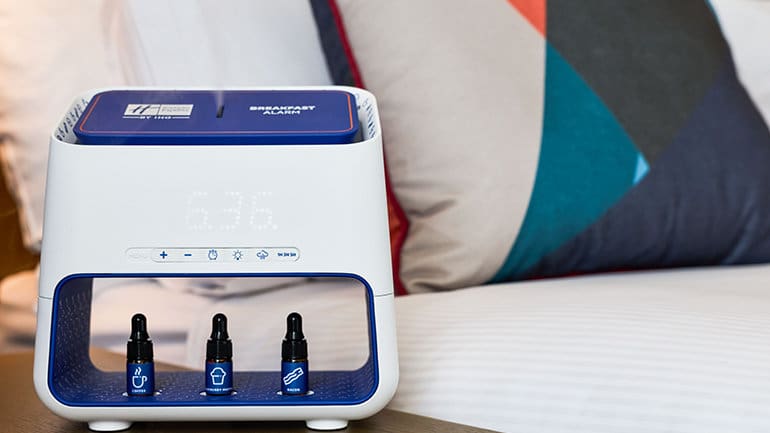 a white and blue alarm clock with two small bottles on a table