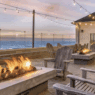 a fire pit and chairs on a deck with a building and a beach