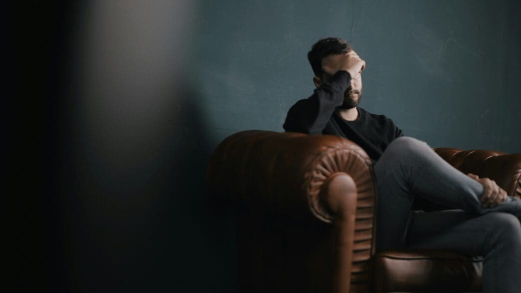 a man sitting on a couch with his hand on his face