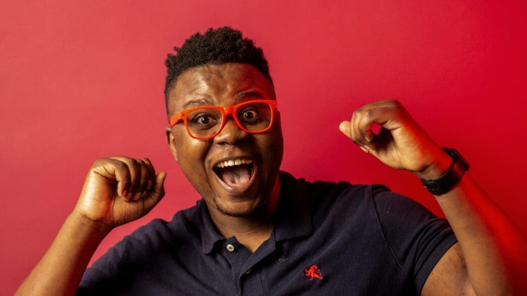 a man with orange glasses and blue shirt with his mouth open