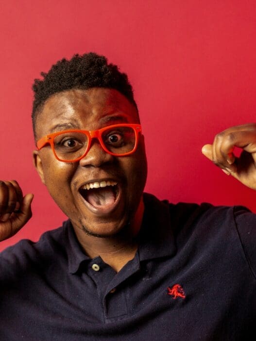 a man with orange glasses and blue shirt with his mouth open