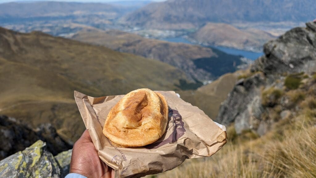 a hand holding a pastry on a paper bag with a view of a valley and mountains