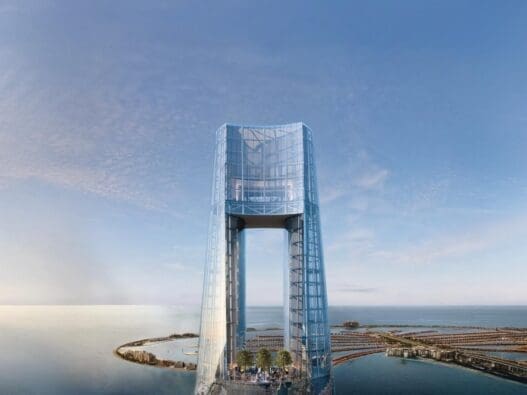 a glass tower with a body of water and a city in the background