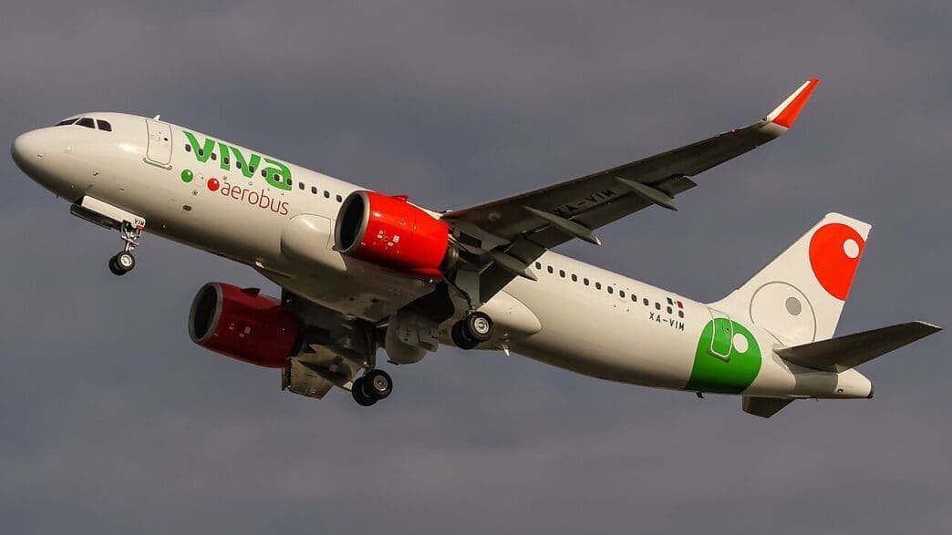 a white airplane with green and red engines flying in the sky