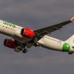 a white airplane with green and red engines flying in the sky