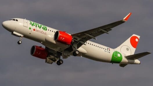 a white airplane with green and red engines flying in the sky