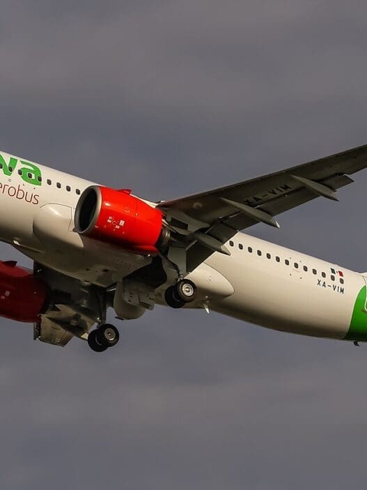 a white airplane with green and red engines flying in the sky