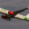 a white airplane with green and red engines flying in the sky