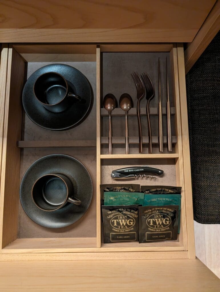 a drawer with a tray of utensils and teacups