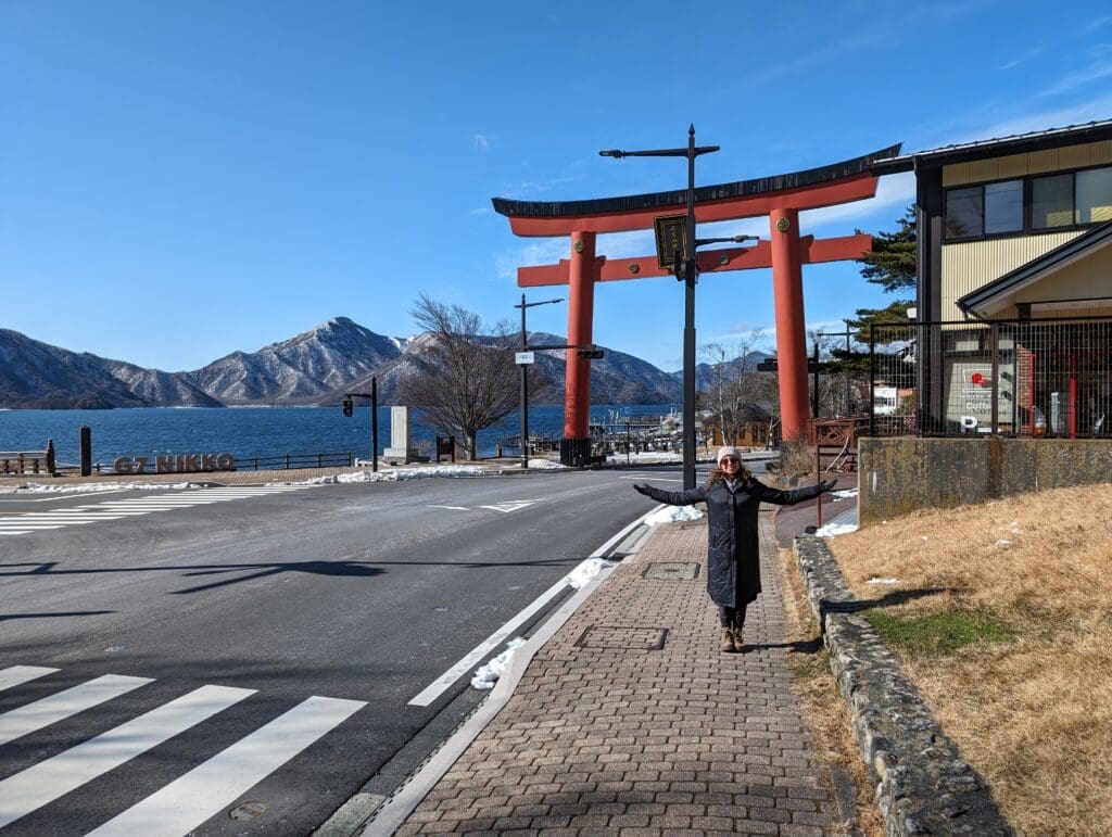 a woman standing on a sidewalk next to a large red arch