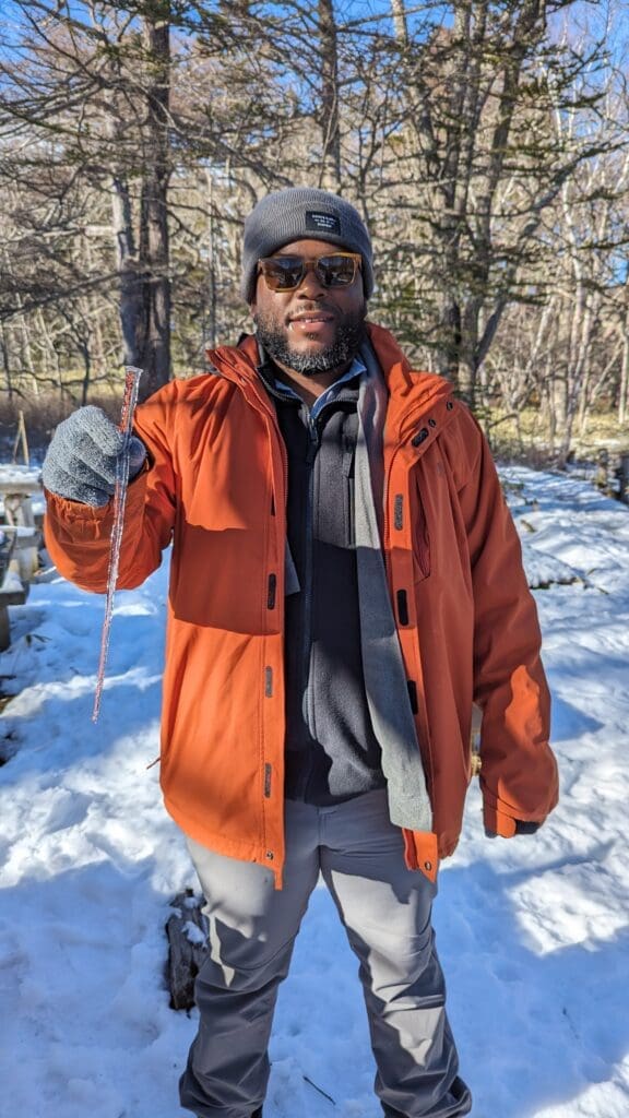 a man in an orange coat and hat holding a stick in the snow