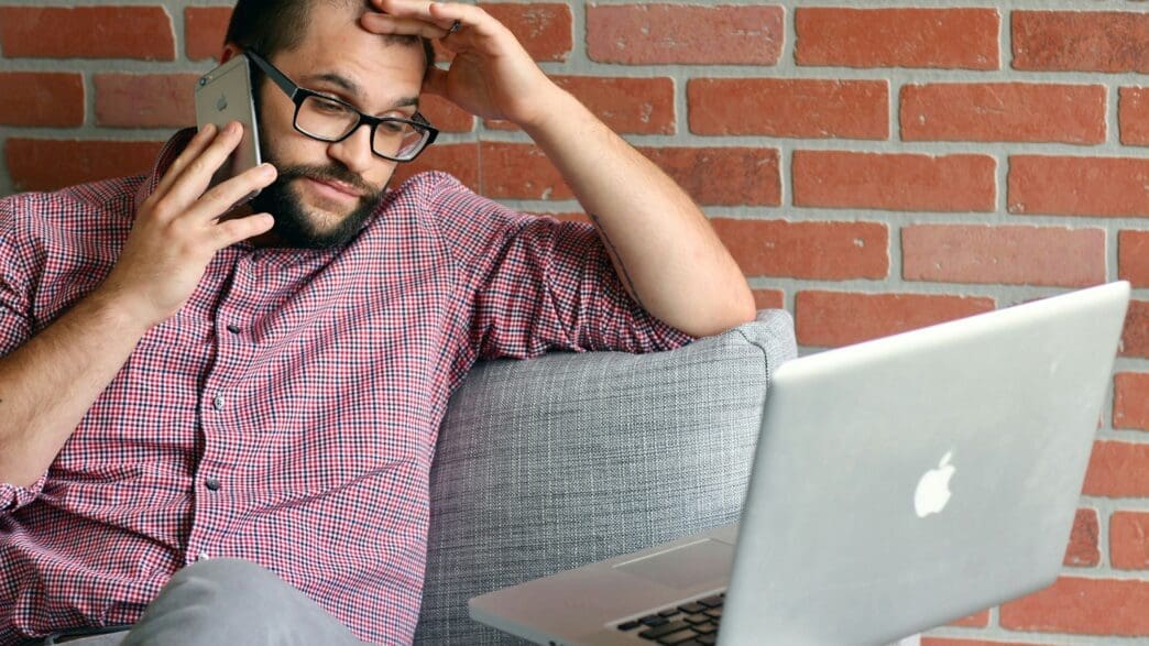 a man sitting on a couch with a laptop and phone