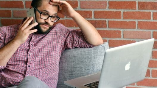 a man sitting on a couch with a laptop and phone