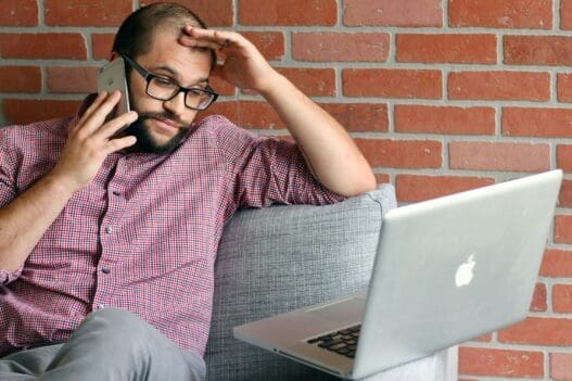 a man sitting on a couch with a laptop and phone