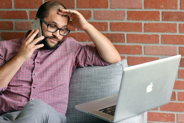 a man sitting on a couch with a laptop and phone