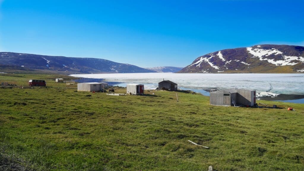 a group of buildings in a grassy area with a body of water and mountains in the background