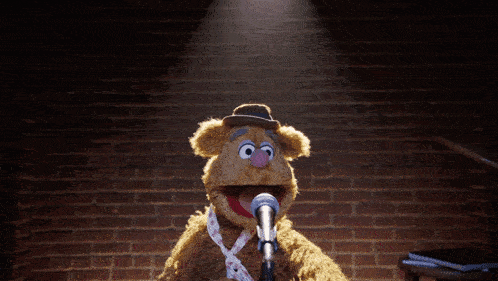 a puppet with a hat and tie speaking into a microphone