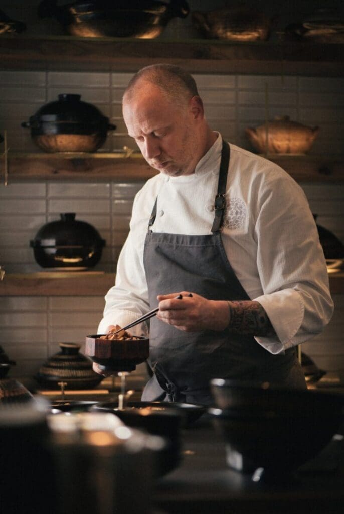 a man in an apron holding chopsticks in a bowl
